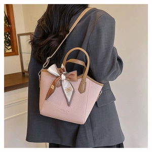Détail du sac seau tissé rose poudré avec anses en cuir marron et foulard décoratif en soie
