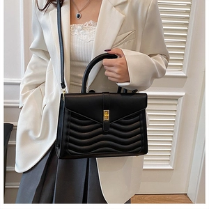 Detail of wave quilted black tote bag with gold twist lock held by model in white suit