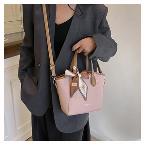 Détail du sac seau rose tressé avec poignées en cuir marron et foulard décoratif en soie