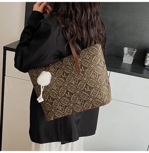Side view of a brown monogram tote bag with M 1981 pattern and a white fur ball charm