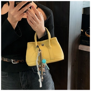 Détail du sac seau en cuir jaune avec breloque décorative et texture litchi
