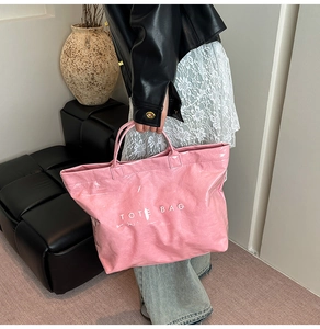 Dettaglio della borsa tote rosa in pelle verniciata lucida con scritta TOTE BAG e manici robusti