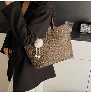 Close-up of brown monogram tote bag with 1981 print and white pompom charm detail
