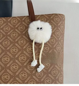 Close-up of a cute white plush doll charm with big eyes hanging on a brown tote bag