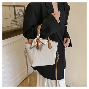 Détail d'un sac seau tissé beige avec poignées en cuir marron et foulard décoratif mode