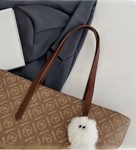 Detail of brown tote bag with vintage monogram patterns and white plush eyeball charm