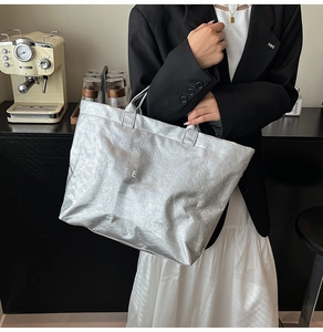 Dettaglio della borsa tote argento metallizzato con texture stropicciata e testo TOTE