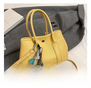 Détail du sac seau en cuir jaune avec breloques décoratives sur un manteau gris