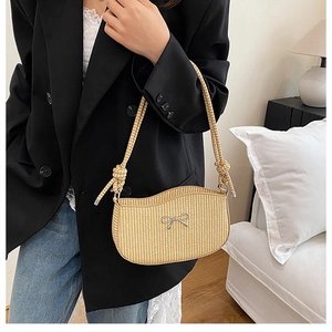 Detail view of woven straw shoulder bag featuring a silver bow and knotted strap