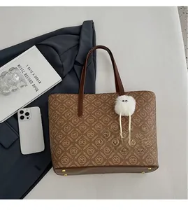 Detailed view of brown tote bag with logo pattern, gold feet, and a cute plush charm