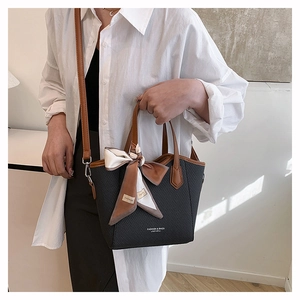 Détail du sac cabas tissé noir avec poignées marron et un foulard en soie décoratif