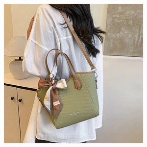Détail du sac seau vert tressé avec bandoulière en cuir marron et foulard décoratif en soie