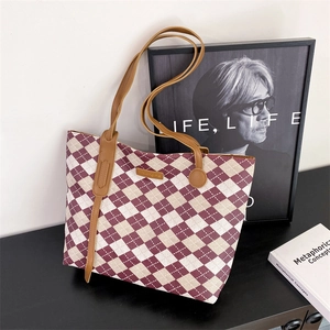 Quilted tote bag in burgundy and beige weave with brown leather handles on a dark desk