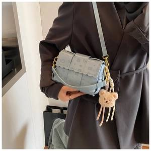 Détail du sac à bandoulière bleu clair avec rabat ondulé et charmant pendentif ours peluche