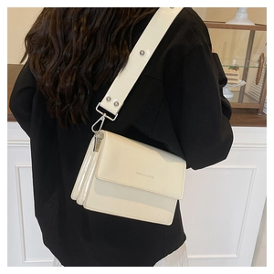Detail of cream white patent leather crossbody bag with wide studded strap on model