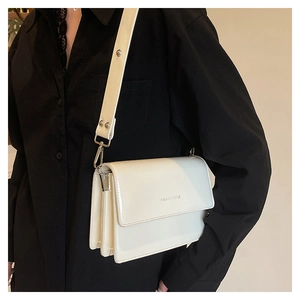 Close-up of white patent leather flap bag with accordion structure and branded strap