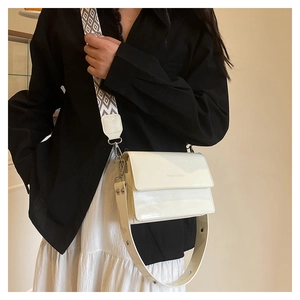 White patent leather crossbody bag with dual straps worn by model against neutral background