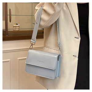 Side view of light blue patent leather flap bag showing accordion pleats and wide strap