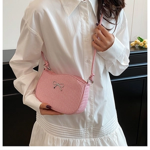 Detail of pink woven crossbody bag with silver metal bow and textured fiber finish
