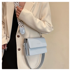 Detail of grey patent leather crossbody bag featuring dual straps and fashion text