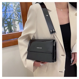 Detail of black patent leather crossbody bag with silver hardware and fashion text