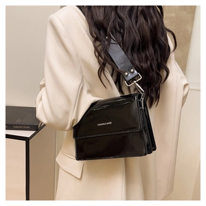 Close-up of a glossy black patent leather crossbody bag with a wide shoulder strap