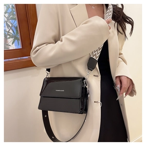 Detail of black patent leather flap bag featuring bold text and geometric woven strap