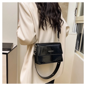 Close-up of black patent leather crossbody bag with white logo and wide shoulder strap