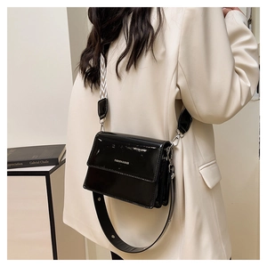 Detail of glossy black patent leather square bag with patterned wide woven strap