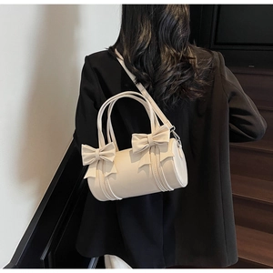 Detailed view of cream bow-decorated cylinder bag worn with a black blazer