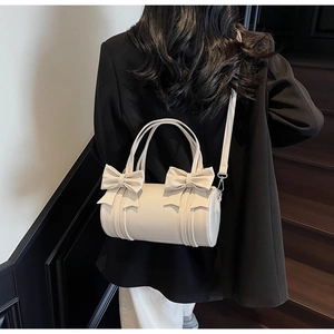 Detail of a beige cylinder bag with elegant bow accents and versatile crossbody strap