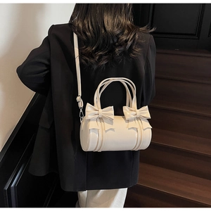 Detail of cream bow-knot cylinder bag shown from behind on a stylish shoulder strap