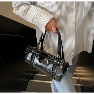 Detail of black patent leather cylinder bag with decorative bow and top handles