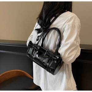 Close-up of black glossy pillow bag featuring dual bow design and slim shoulder straps