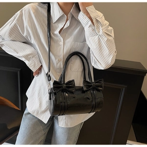 Detail of glossy black patent leather barrel bag with bow decor worn by a model
