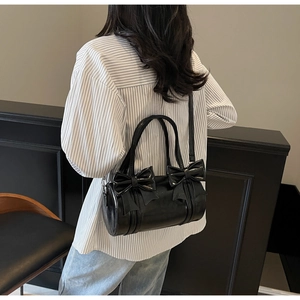 Detail of black glossy leather Boston bag featuring decorative bow accents on the side