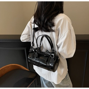 Detail of a black cylinder handbag with sweet bow accents and a glossy finish