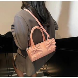 Detailed view of pink cylinder bow bag with long strap paired with a grey blazer