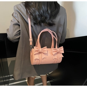 Rear view of a model wearing a pink bow cylinder handbag with detachable shoulder strap