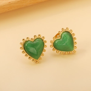 Détail macro de boucles d'oreilles cœur dorées perlées avec pierre œil de chat verte