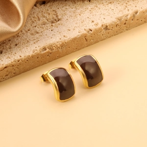 Détail de boucles d'oreilles rectangulaires en or et émail marron sur pierre travertin