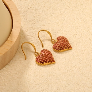 Boucles d'oreilles cœur en or 18K avec strass roses sur une surface texturée beige