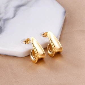 Detail view of gold irregular J-shaped stud earrings on white marble display