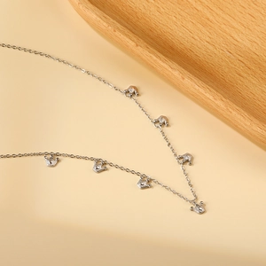Dettaglio di ciondoli a corona in argento su catena in acciaio su sfondo beige
