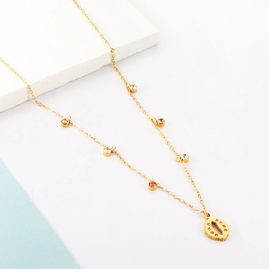 Detailed close-up of golden shell pendant necklace with colorful gemstones on a textured stone