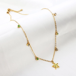 Detail of gold necklace with star pendant and green gemstones on white fabric