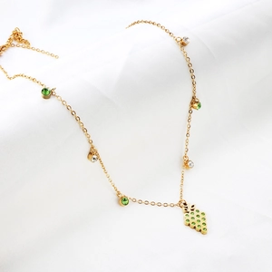 Detailed macro of gold grape pendant necklace with green crystals on white fabric