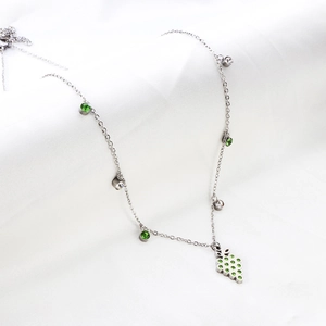 Close-up of silver grape pendant necklace with green crystals on textured white fabric