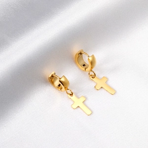 Boucles d'oreilles créoles croix en acier doré sur un élégant fond de soie blanche satinée