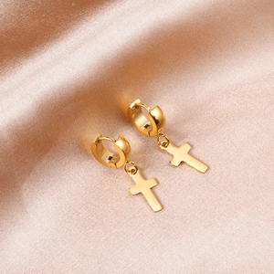 Détail macro des boucles d'oreilles croix dorées polies sur un tissu en soie champagne